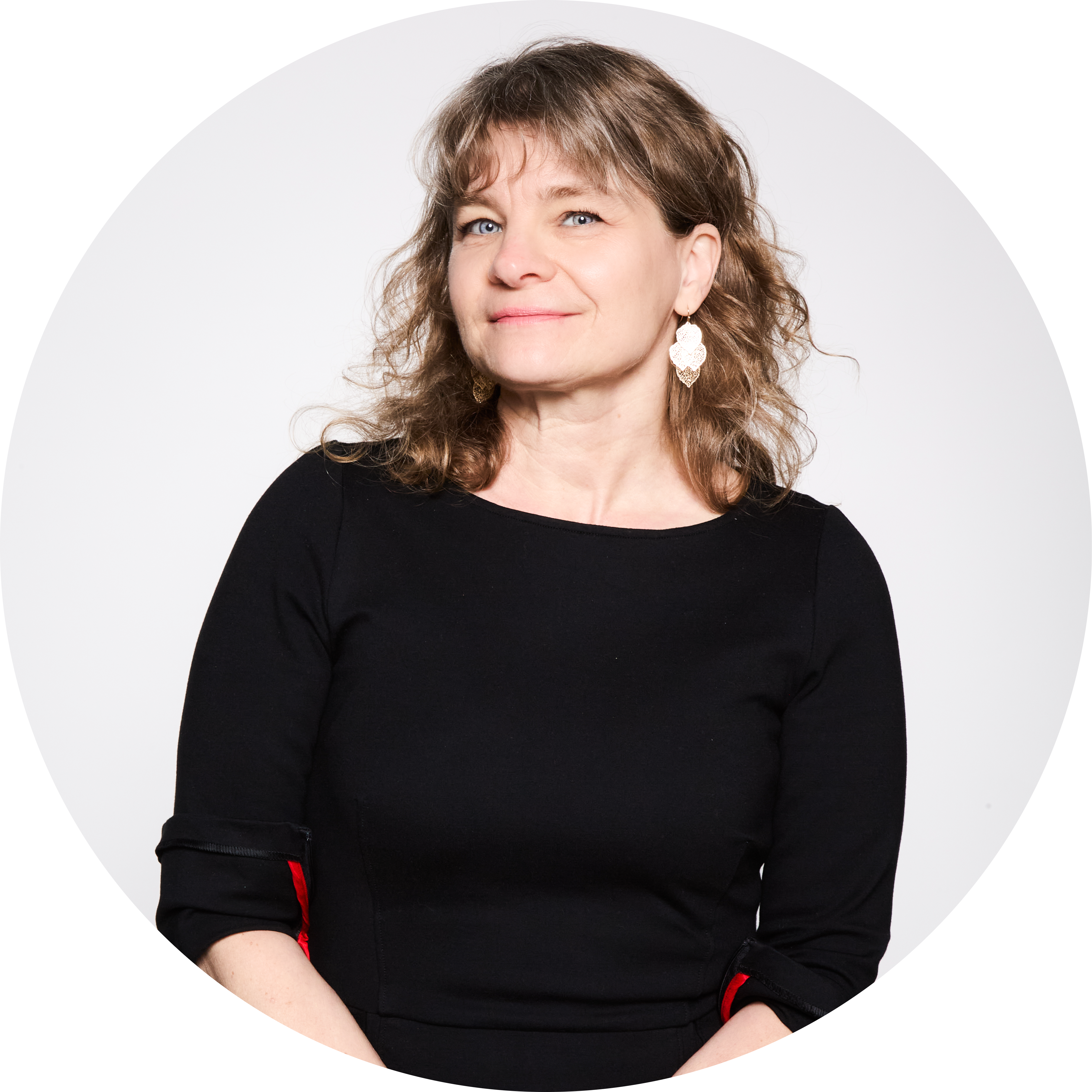 Sonya Geis with wavy brown hair wearing a black dress with red accents and decorative earrings against a white background.