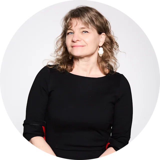 Sonya Geis with wavy brown hair wearing a black dress with red accents and decorative earrings against a white background.