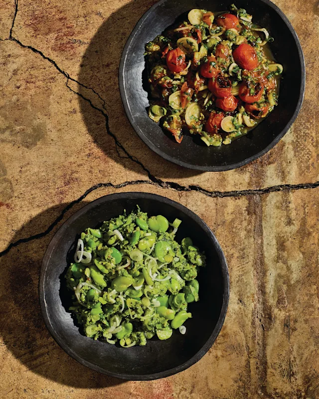 Two black bowls on stone surface - top with roasted tomato vegetable mix, bottom with bright green bean salad.