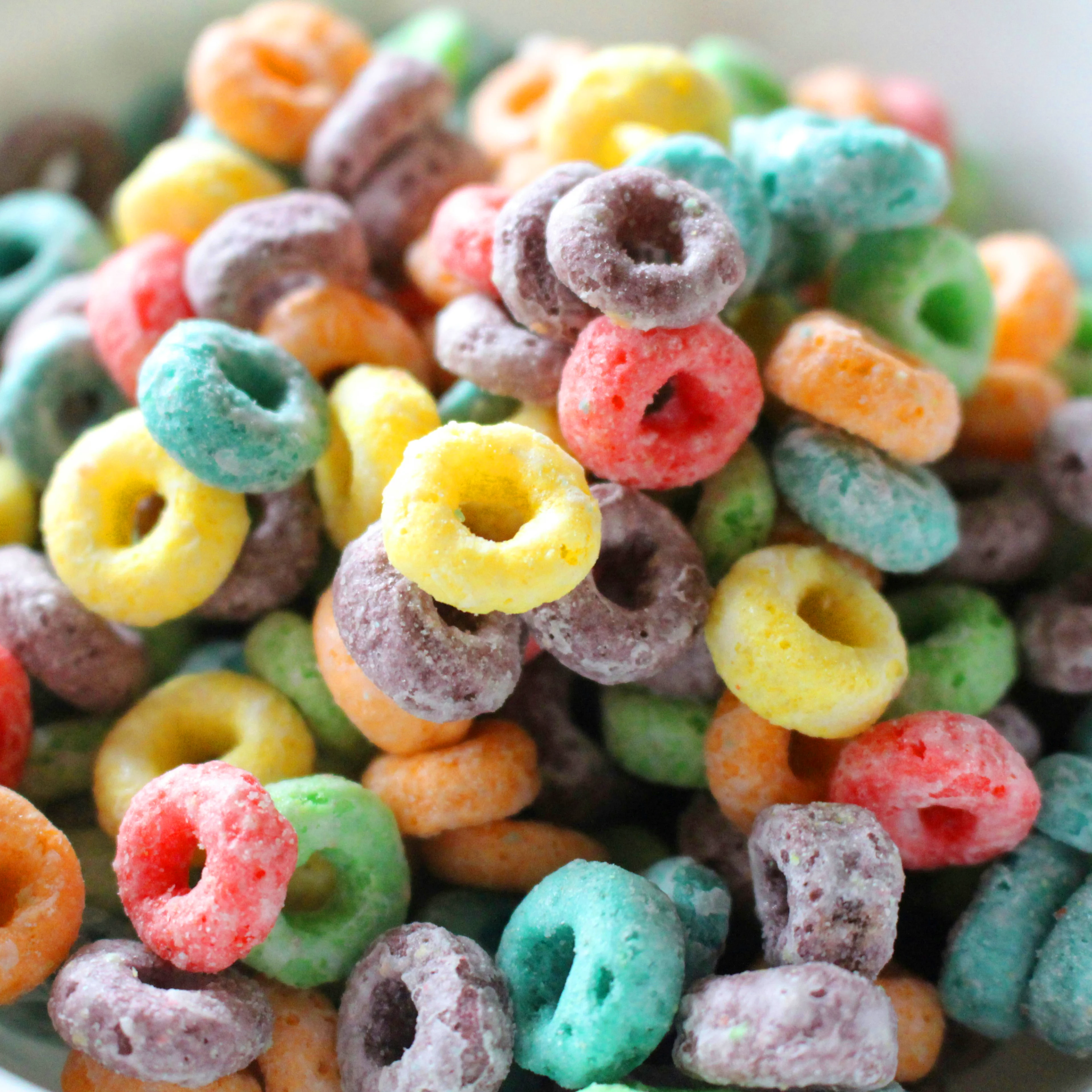 A white bowl filled with colorful fruit-flavored cereal loops in red, yellow, green, orange, teal, and purple hues.