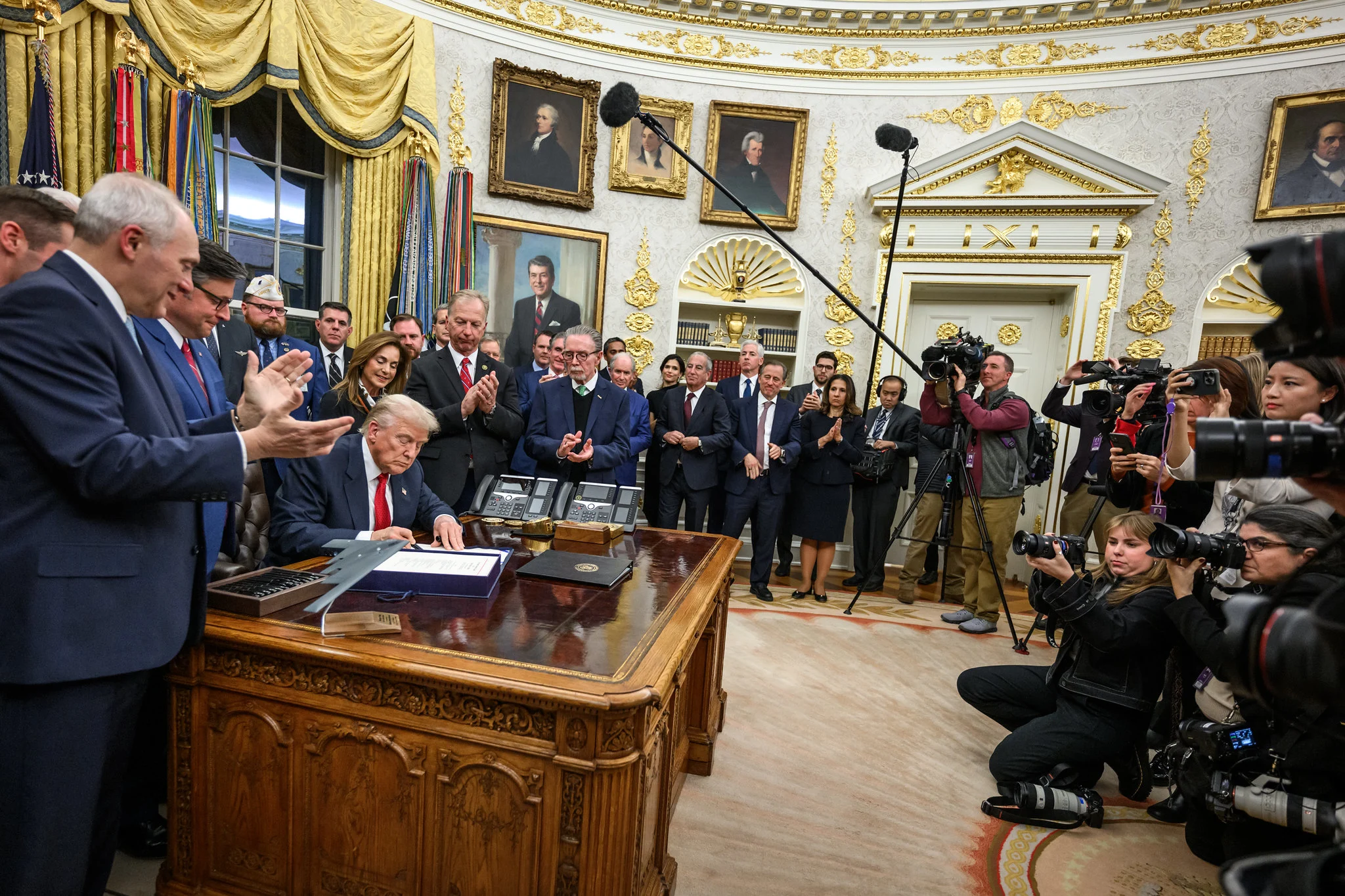 President Trump sits at the resolute desk surrounded by people