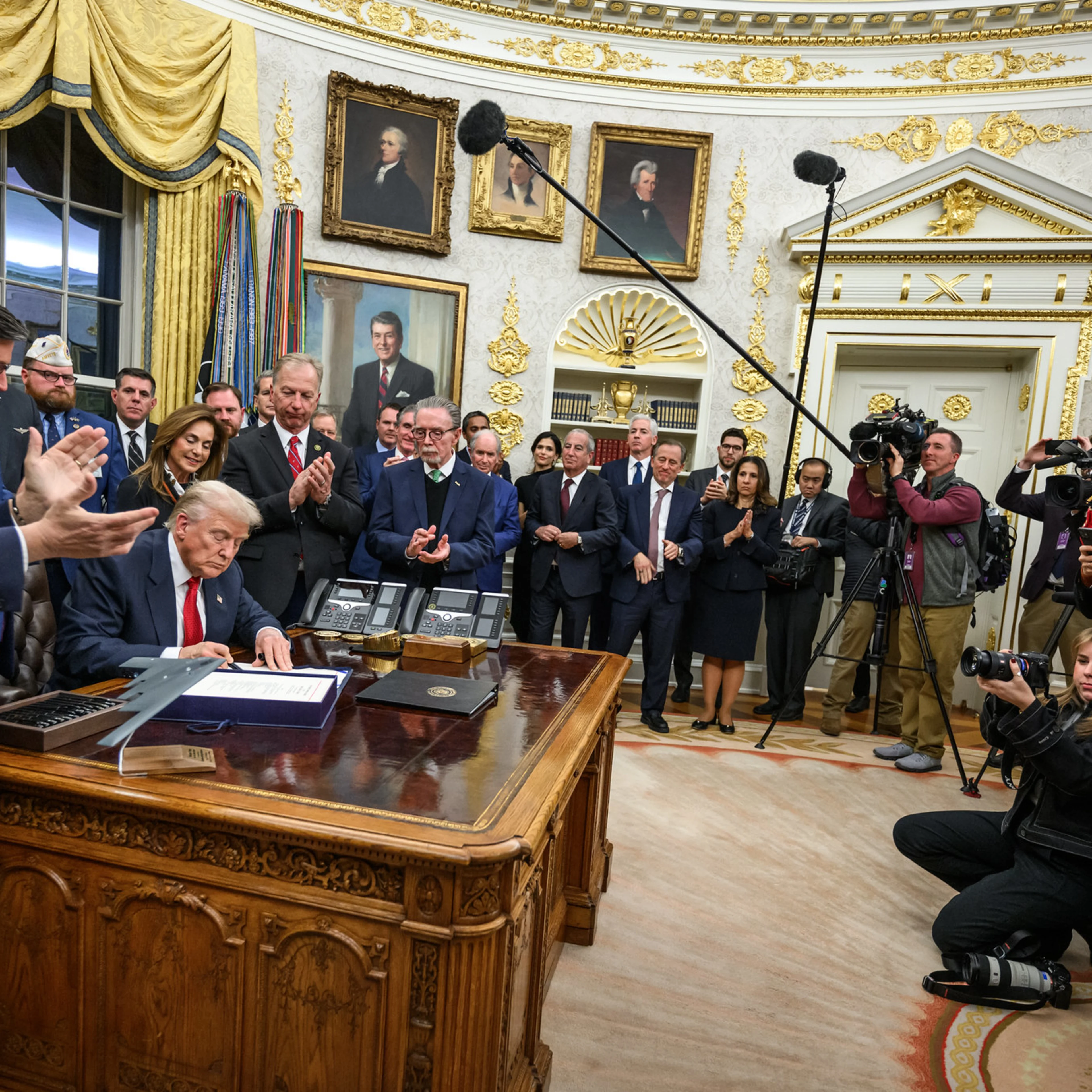 President Trump sits at the resolute desk surrounded by people
