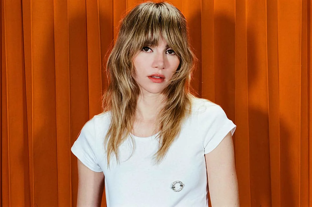 Press photo of Suki Waterhouse in front of an orange background