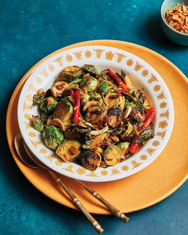 Roasted Brussels sprouts with red peppers and onions on a decorative plate with gold trim, served on an orange charger.