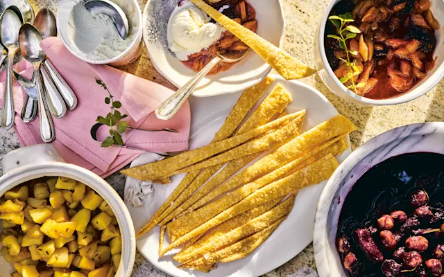 A dessert spread with golden pastry strips, fruit compotes, ice cream, and silver spoons on pink linen napkins.