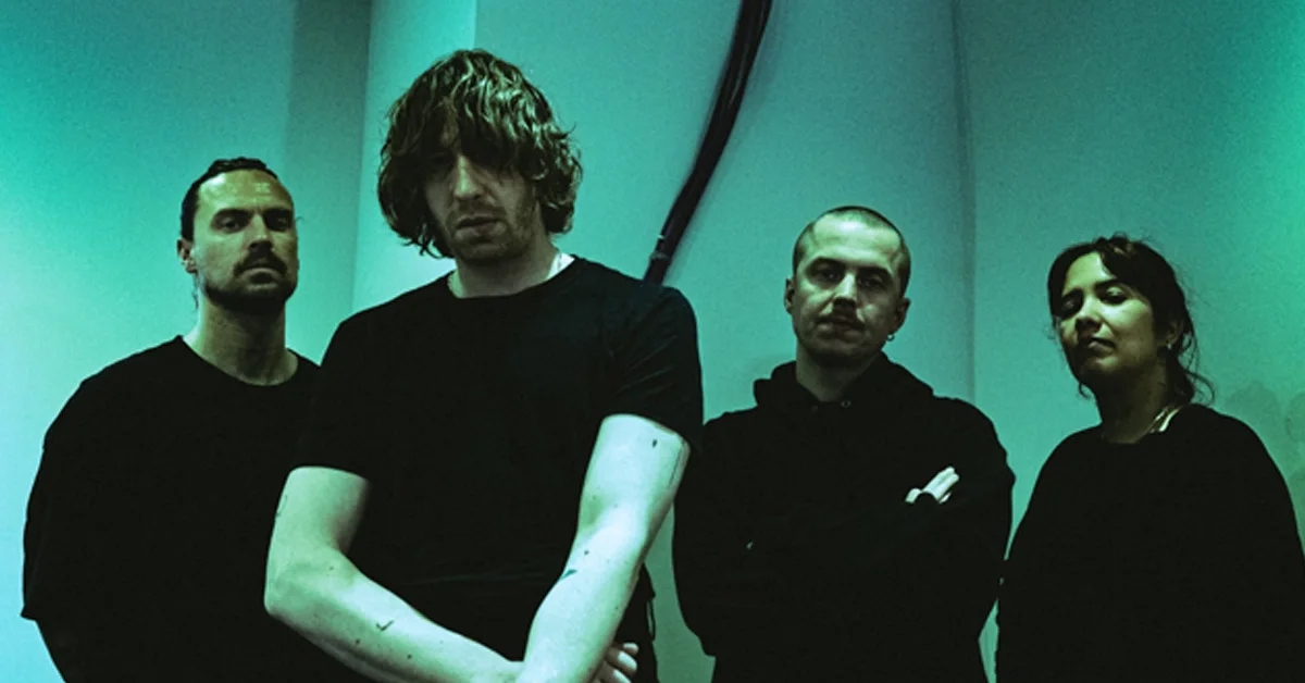 Four people dressed in black pose seriously against a teal-lit wall.