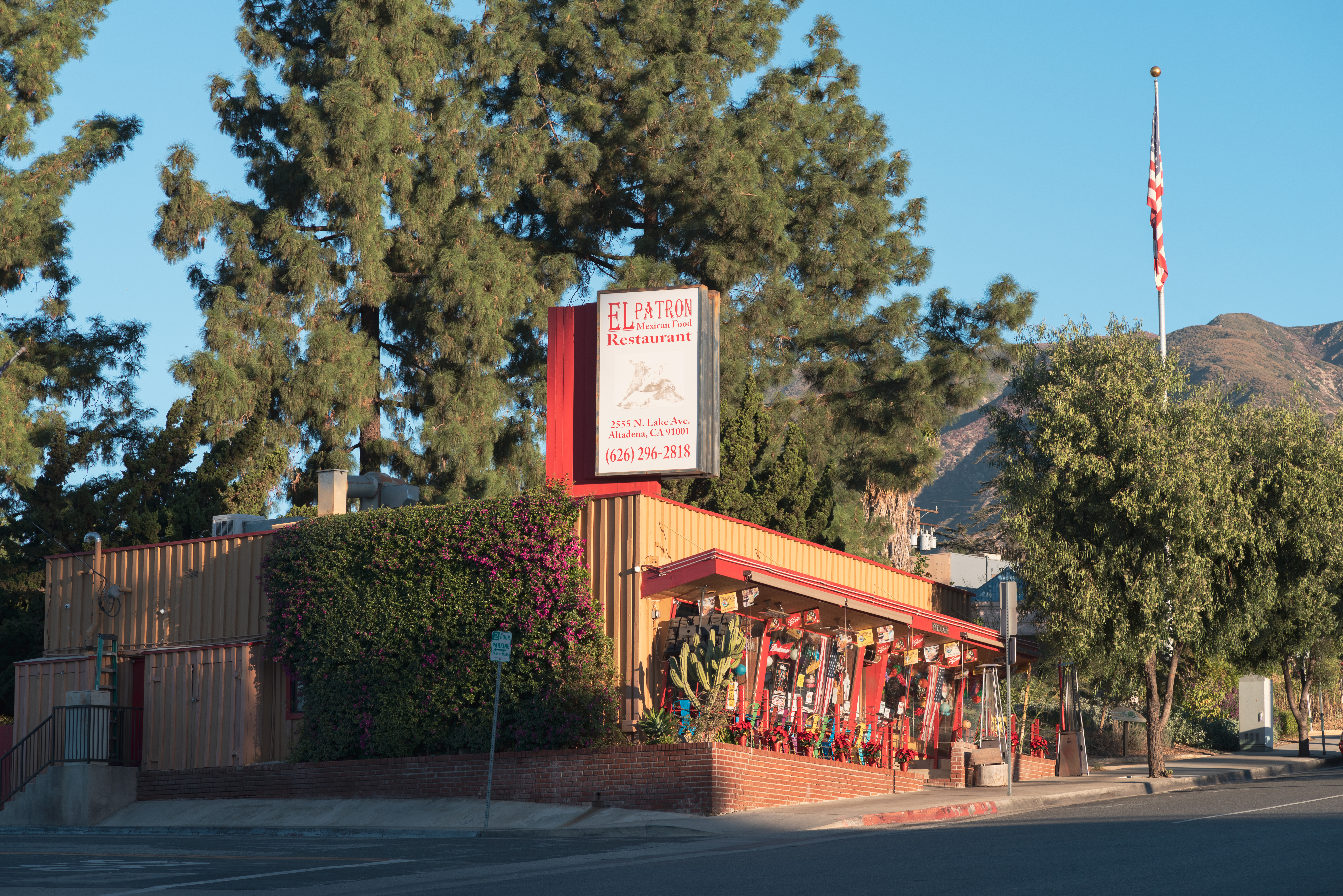 El Patron Mexican restaurant with red trim exterior, surrounded by pine trees and mountains, with American flag nearby.