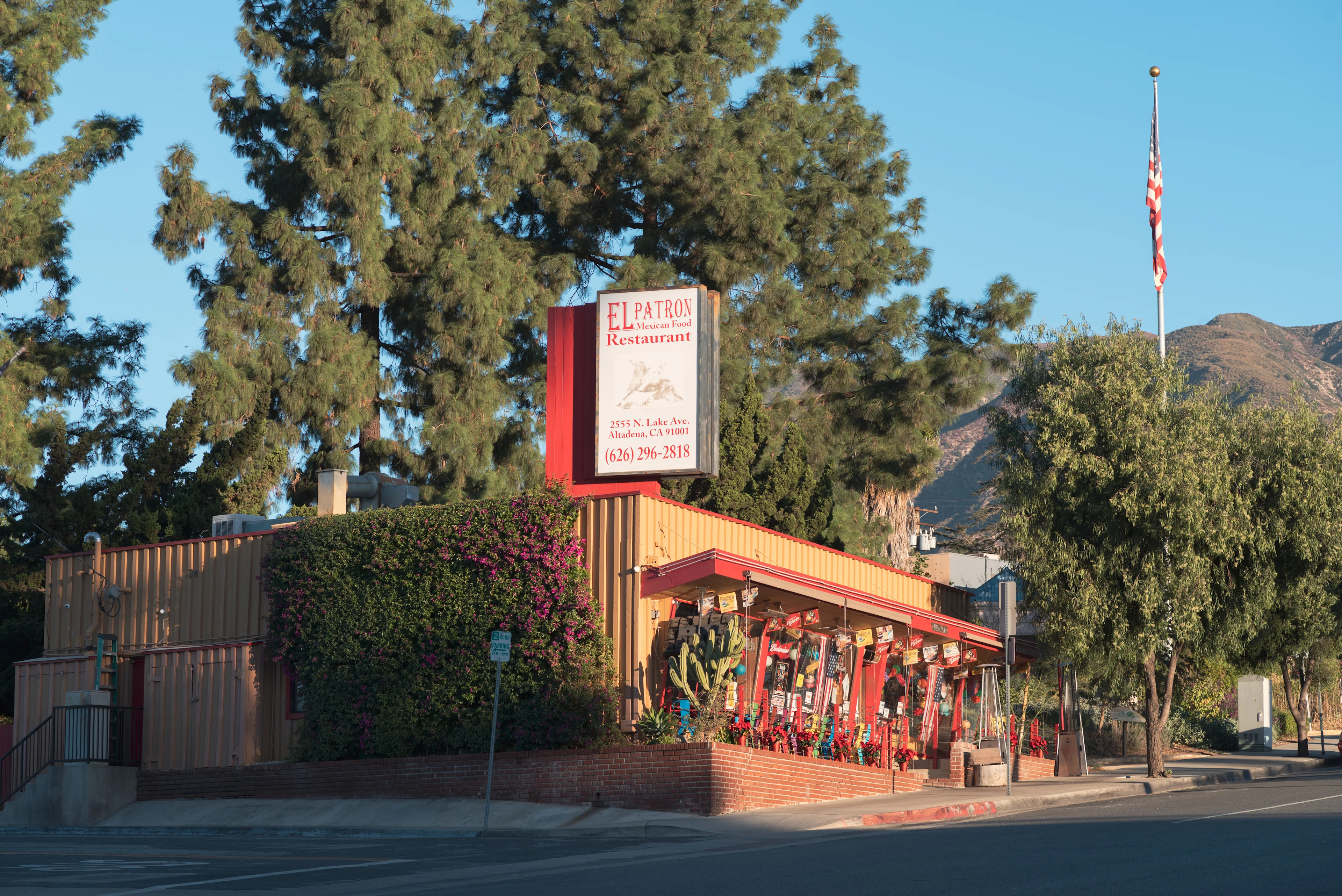 El Patron Mexican restaurant with red trim exterior, surrounded by pine trees and mountains, with American flag nearby.