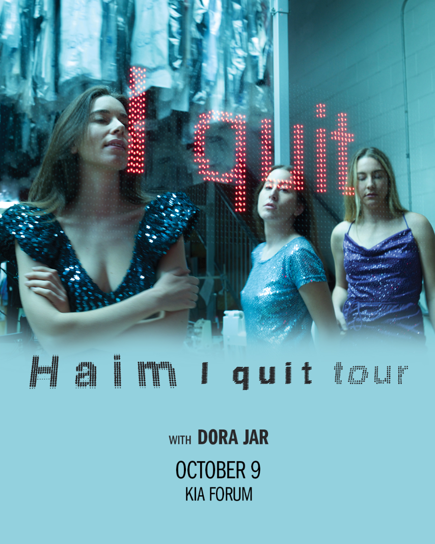 Three people in sparkly dresses with red "I quit" sign, promoting Haim I quit tour on October 9 at KIA Forum with Dora Jar.
