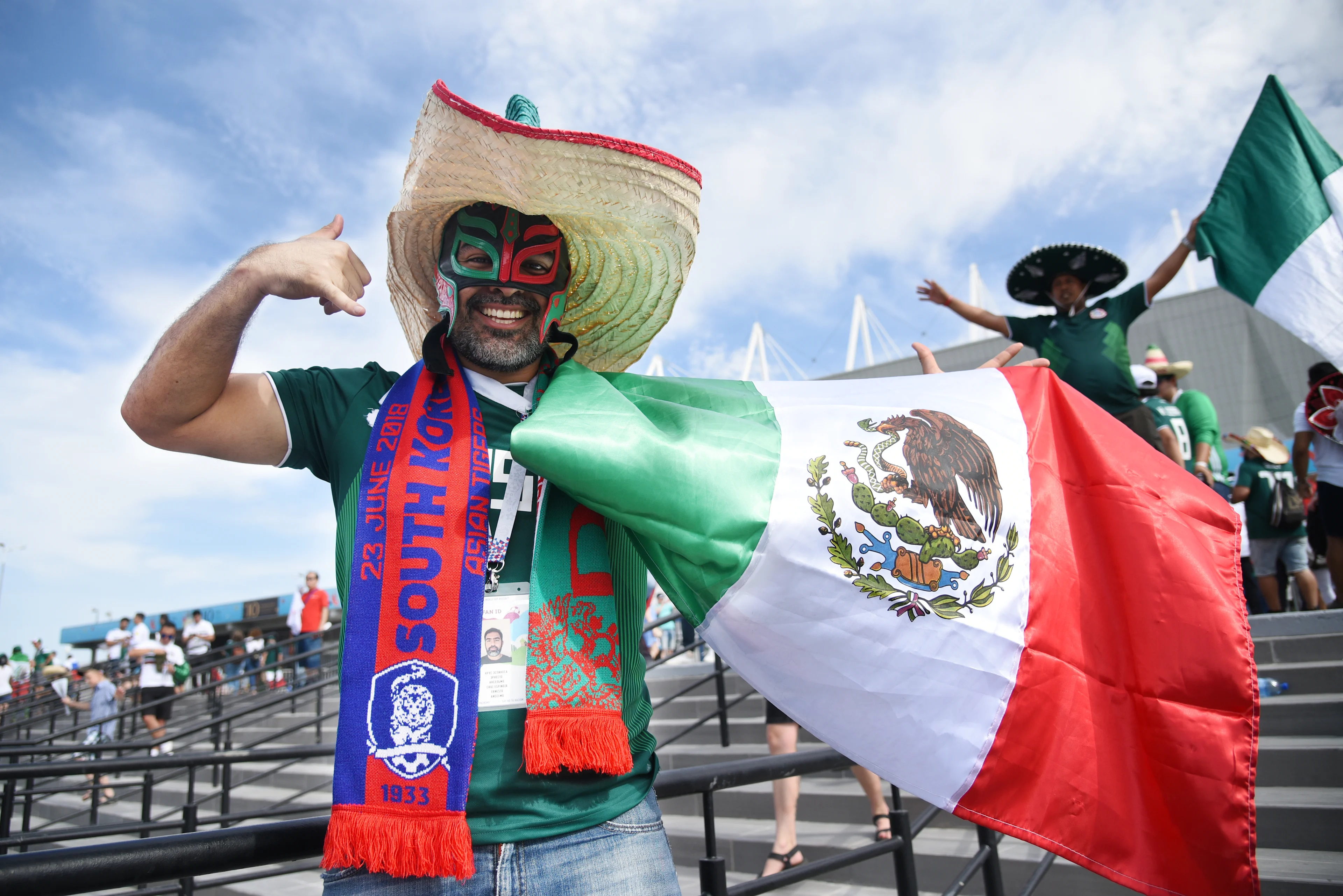 A man in a Mexico National Soccer Team jersey holds a Mexico Flag.