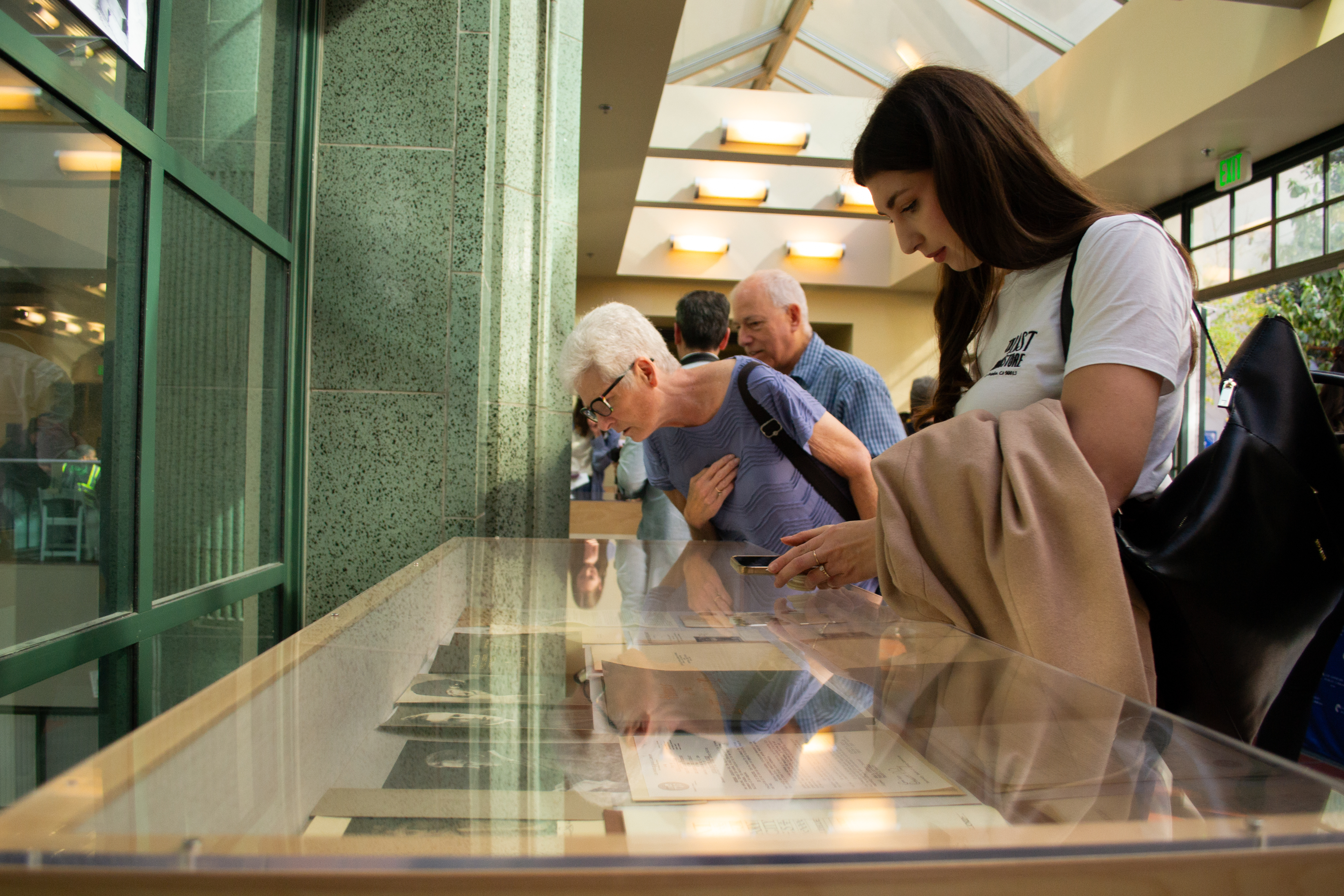Three people look at some of the historical records and documents in a glass display case that were pulled from a time capsule buried in the LA Central Library in 1925.