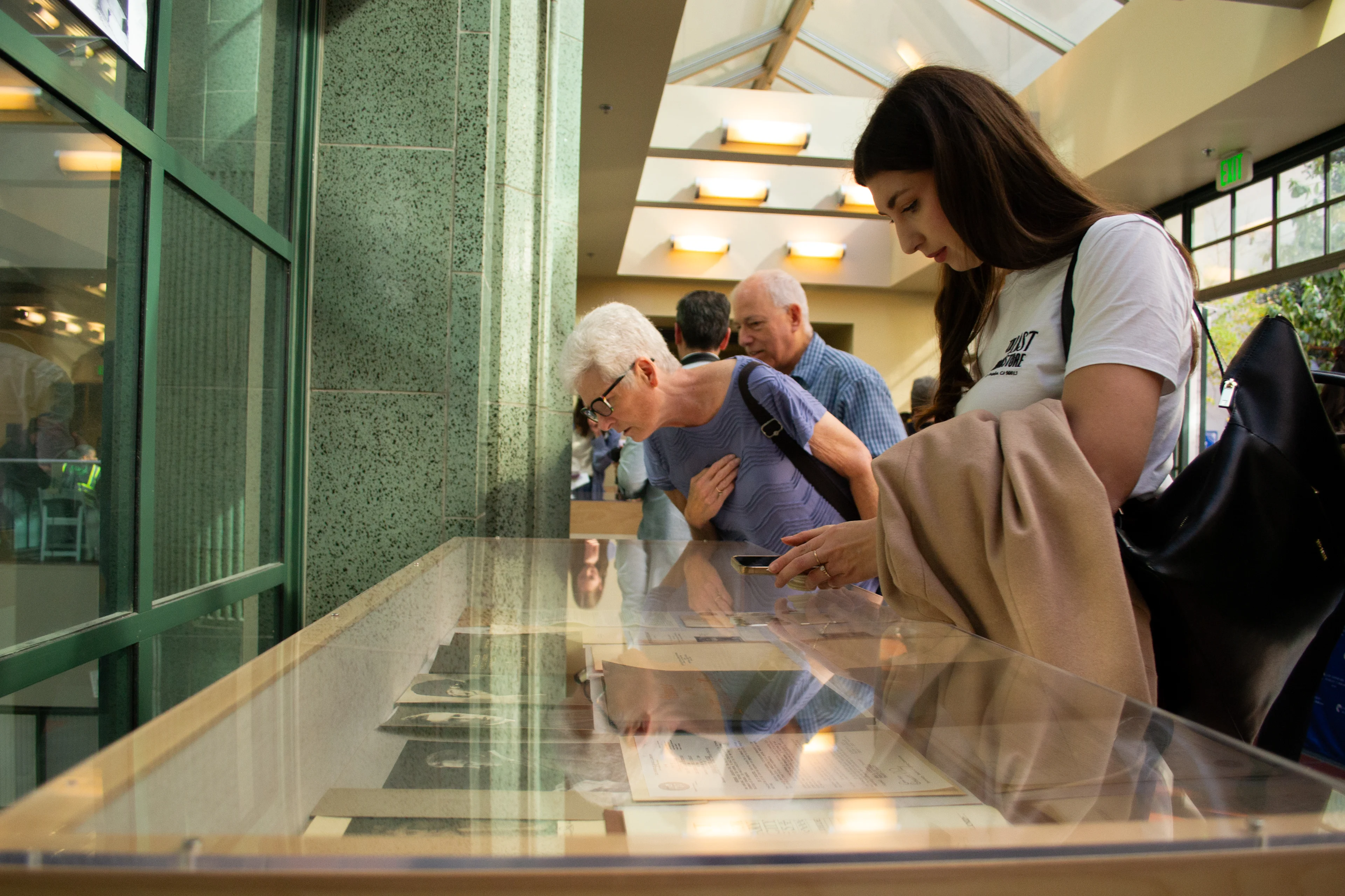 Three people look at some of the historical records and documents in a glass display case that were pulled from a time capsule buried in the LA Central Library in 1925.