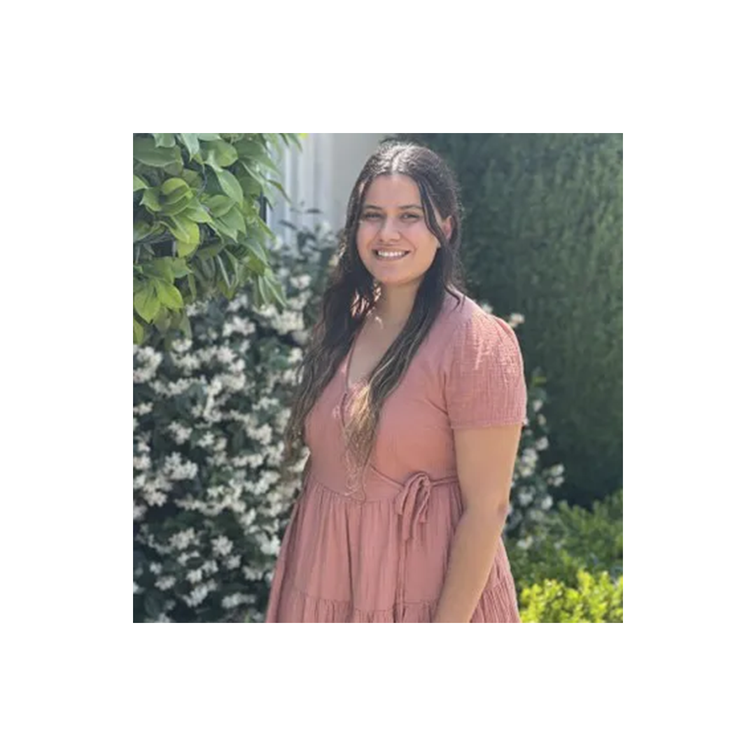 Person in pink dress smiling outdoors with green foliage and white flowering plants in background