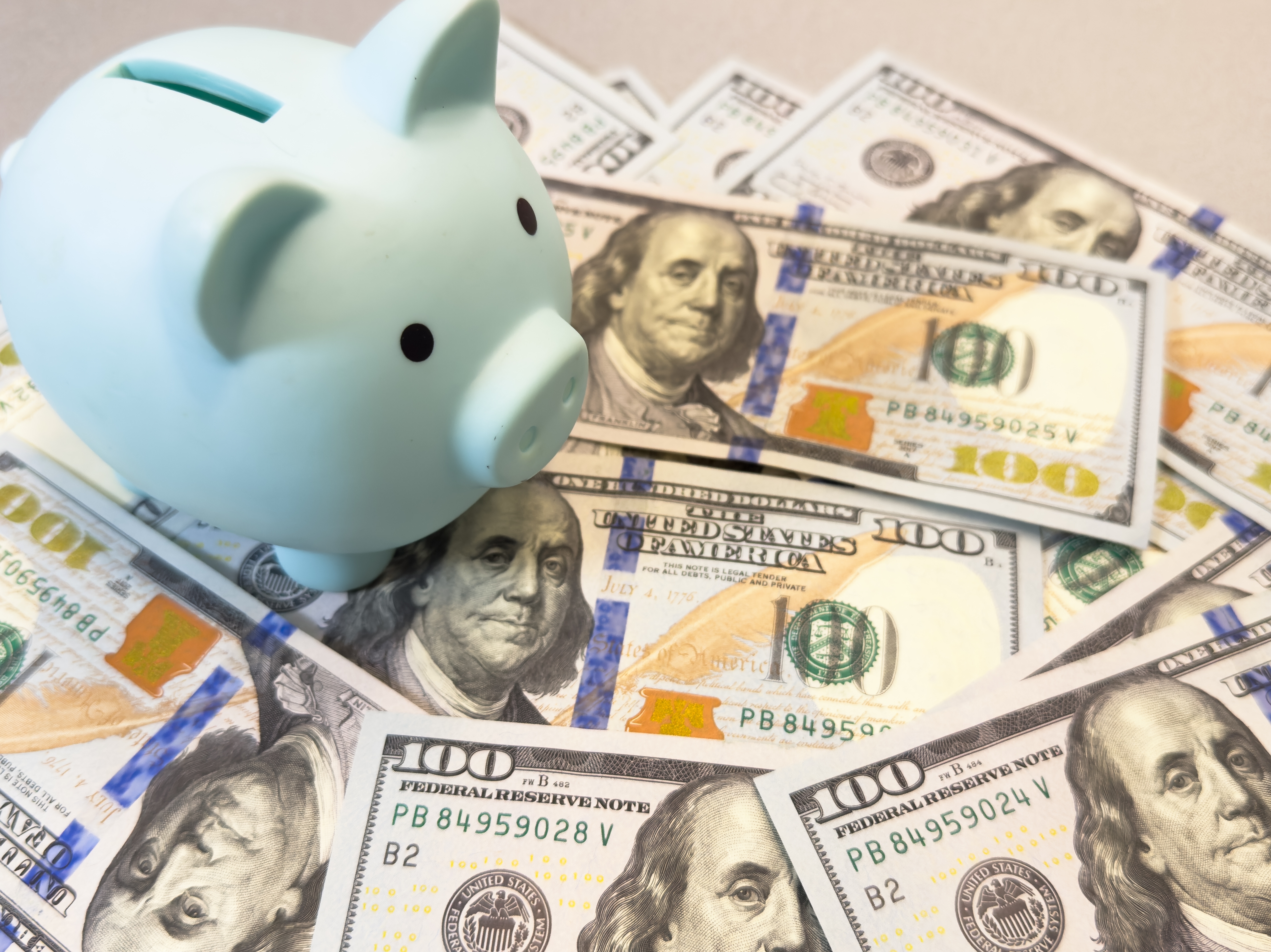 A blue piggy bank sits on a spread of 100 dollar bills