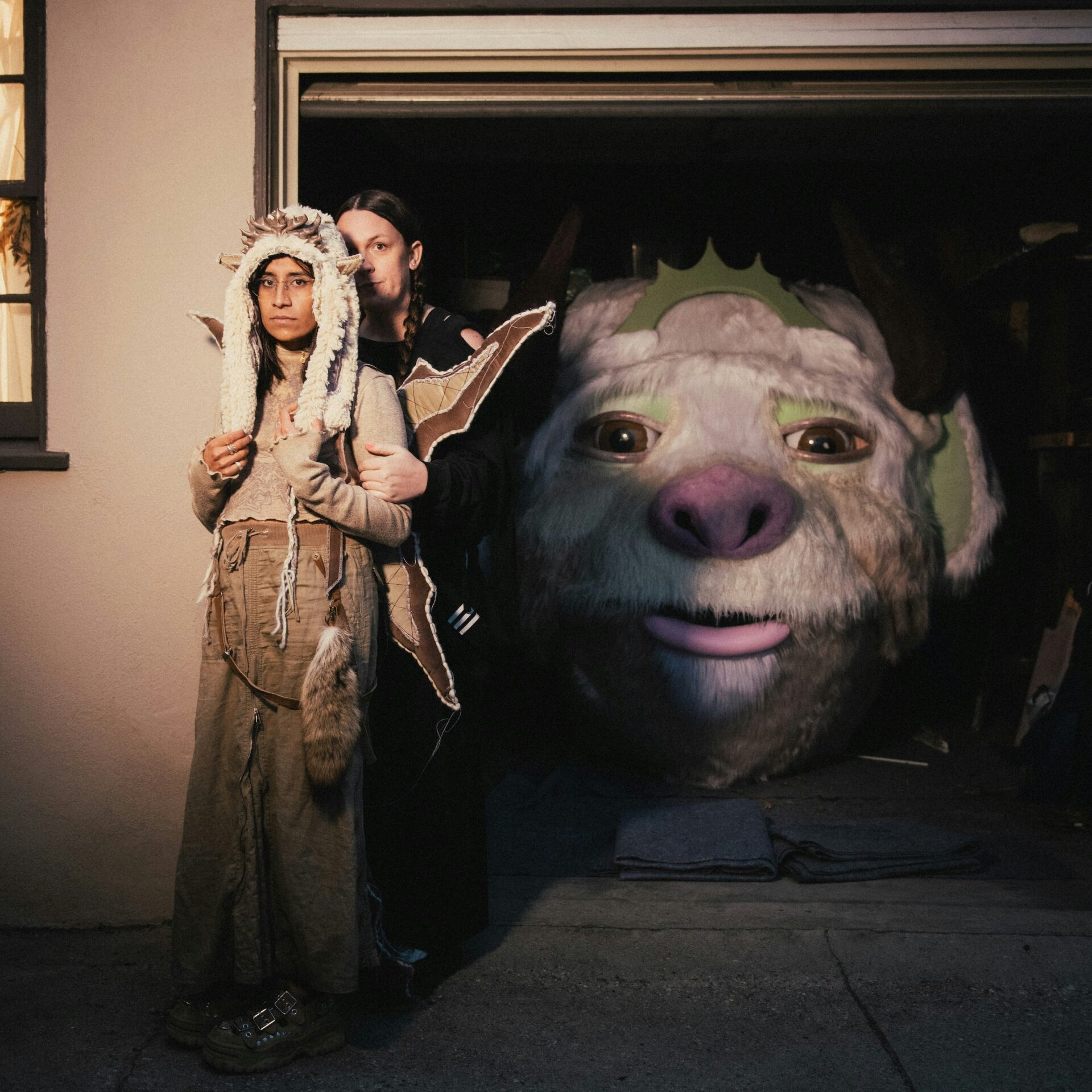 Person in Native American-inspired costume standing beside a large fantasy creature puppet with a furry face and pink nose.
