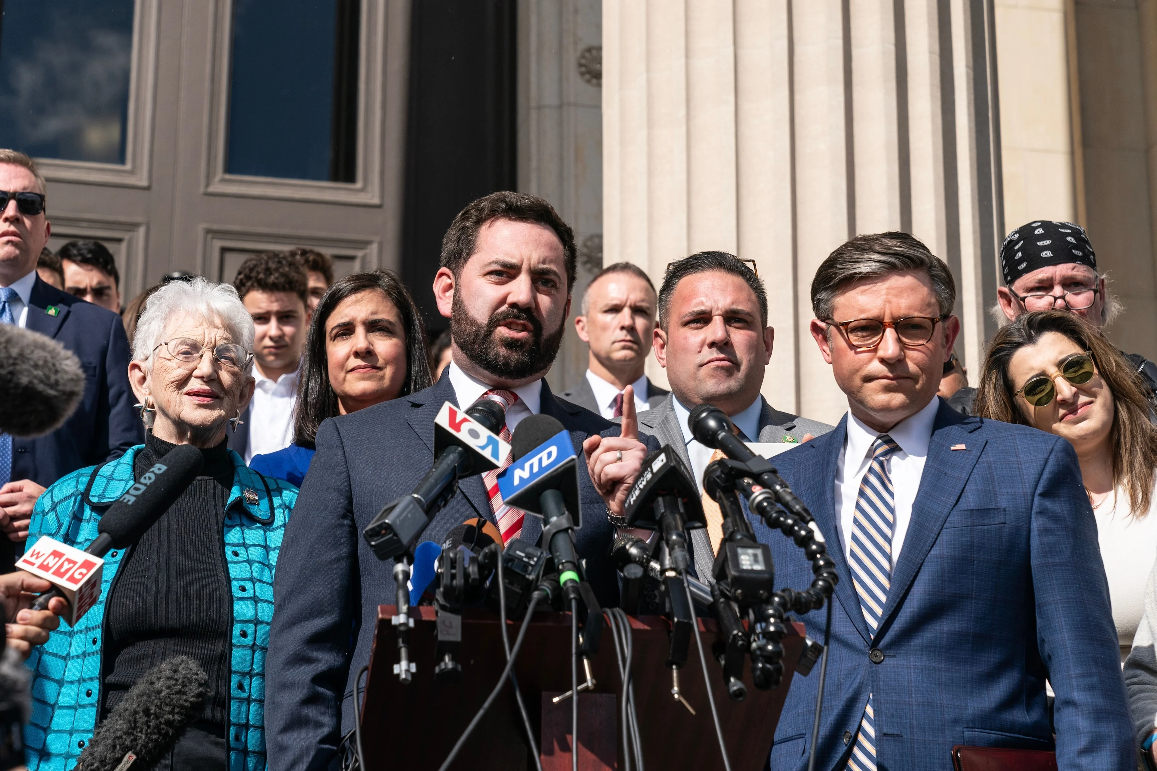 Two men stand in front of a podium and microphones