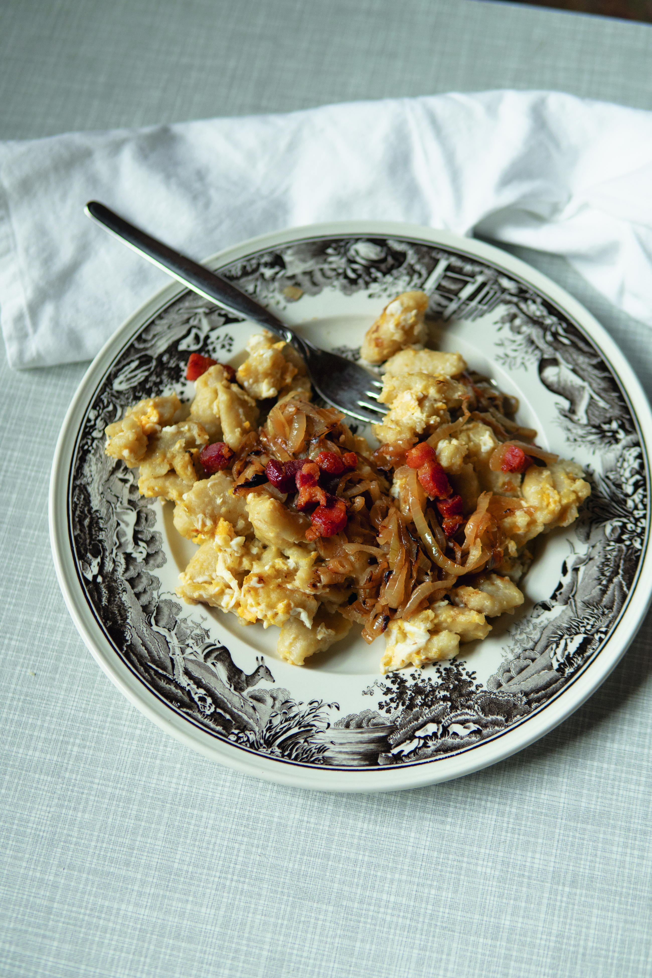 Scrambled eggs with caramelized onions and bacon bits served on a decorative plate with a fork.