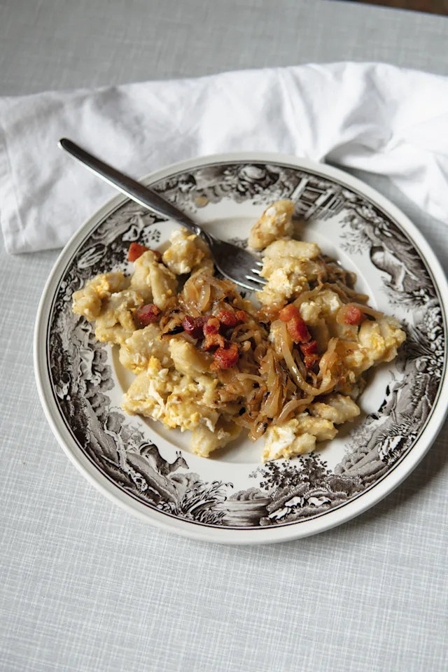 Scrambled eggs with caramelized onions and bacon bits served on a decorative plate with a fork.