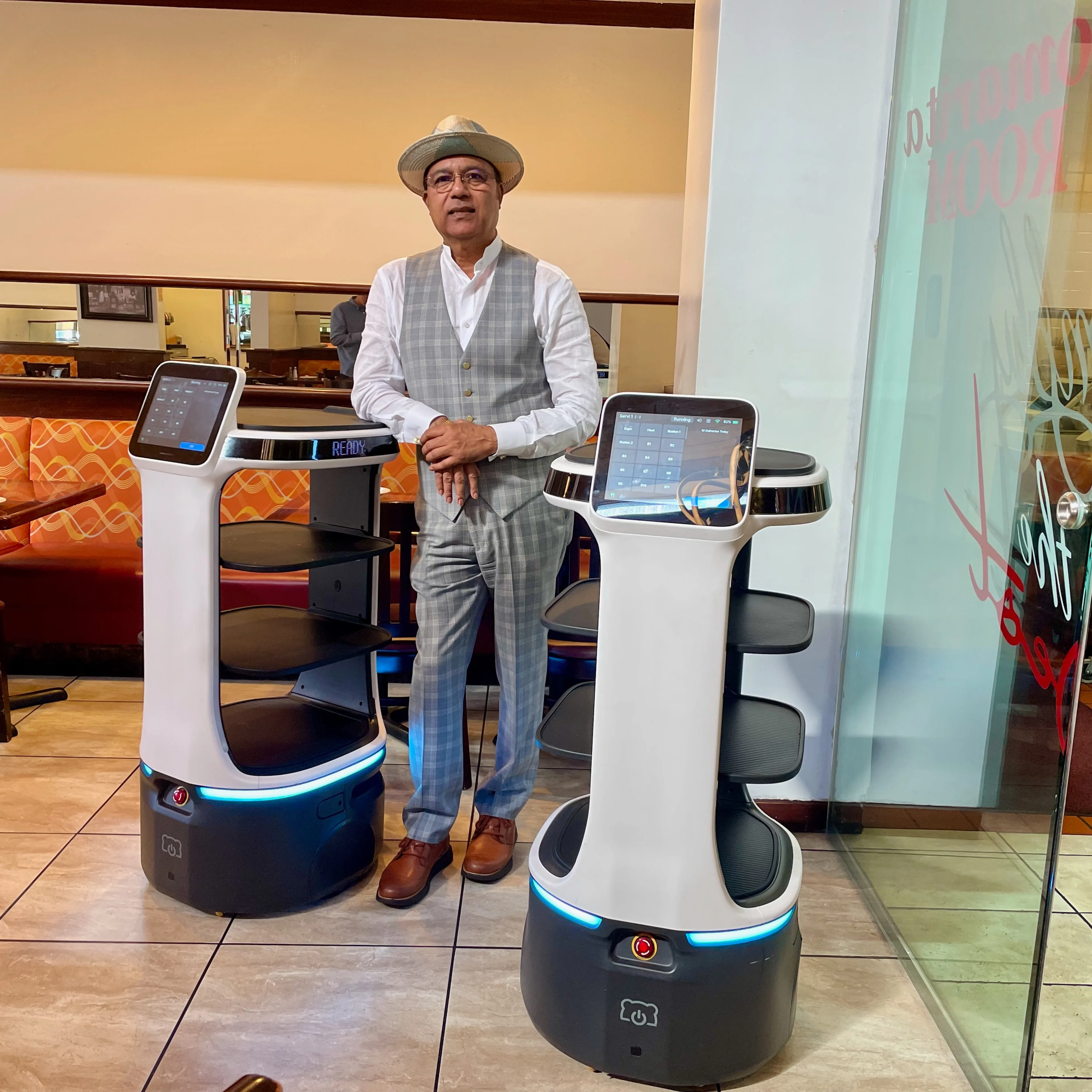 A man stands in the middle of two robot servers inside of a restaurant
