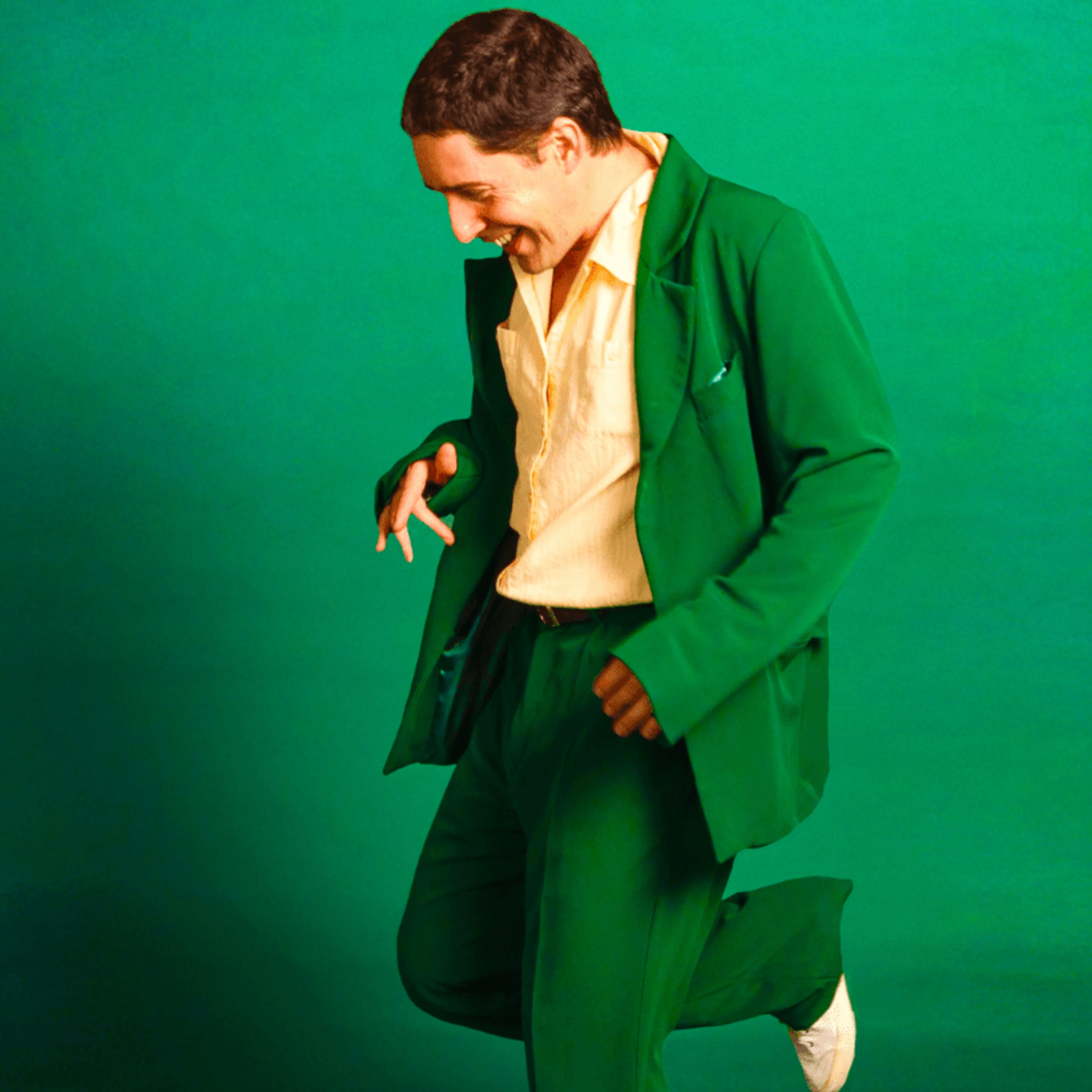Person in bright green suit with cream shirt smiling and dancing against a vibrant green background.