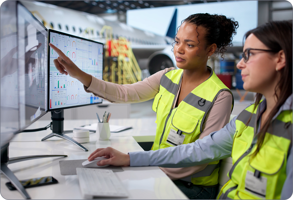 Industries and applications - Visual Two engineers in safety vests review data dashboards on a monitor inside an aircraft hangar.