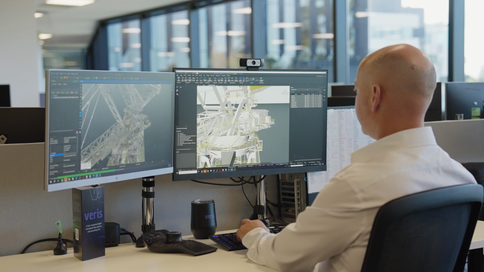 Veris - BricsCAD Customer Story Person working at dual monitors displaying BricsCAD interface with 3D industrial structure models in a modern office.