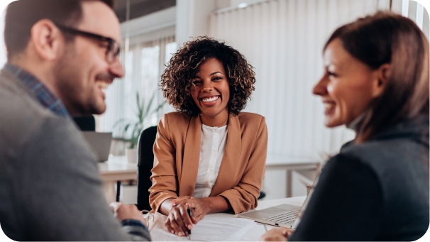 Three colleagues smiling and engaged in a friendly discussion around a table in a bright office setting.