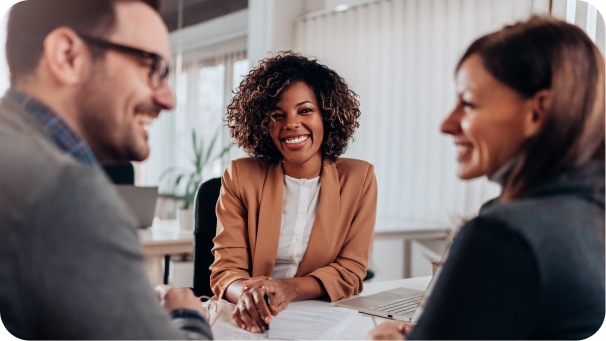 Genuine business relationship - Thumbnail Three colleagues smiling and engaged in a friendly discussion around a table in a bright office setting.