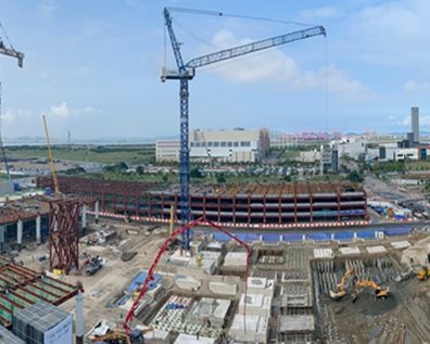 Aerial view of a large construction site with a tower crane, curved steel structure, and heavy machinery in an urban area.