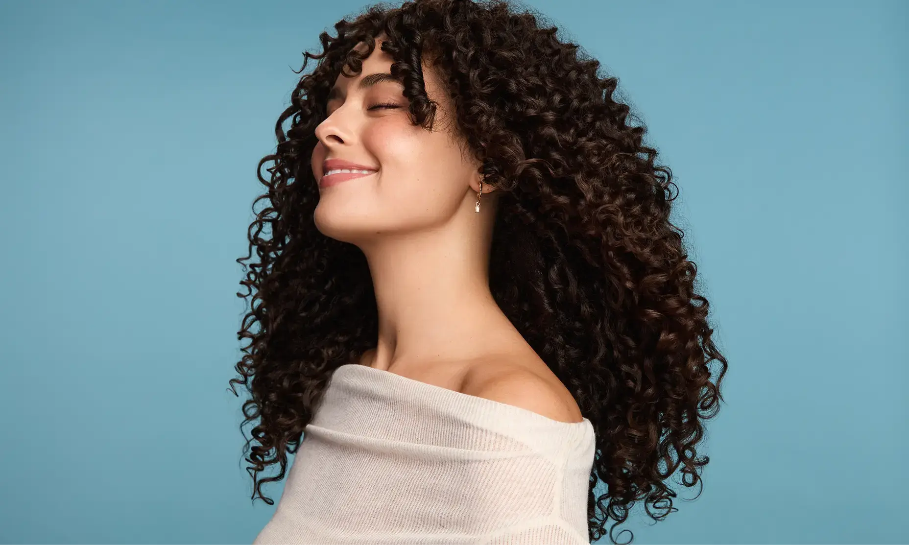 Woman with coily hair smiling after using Maui Moisture® products