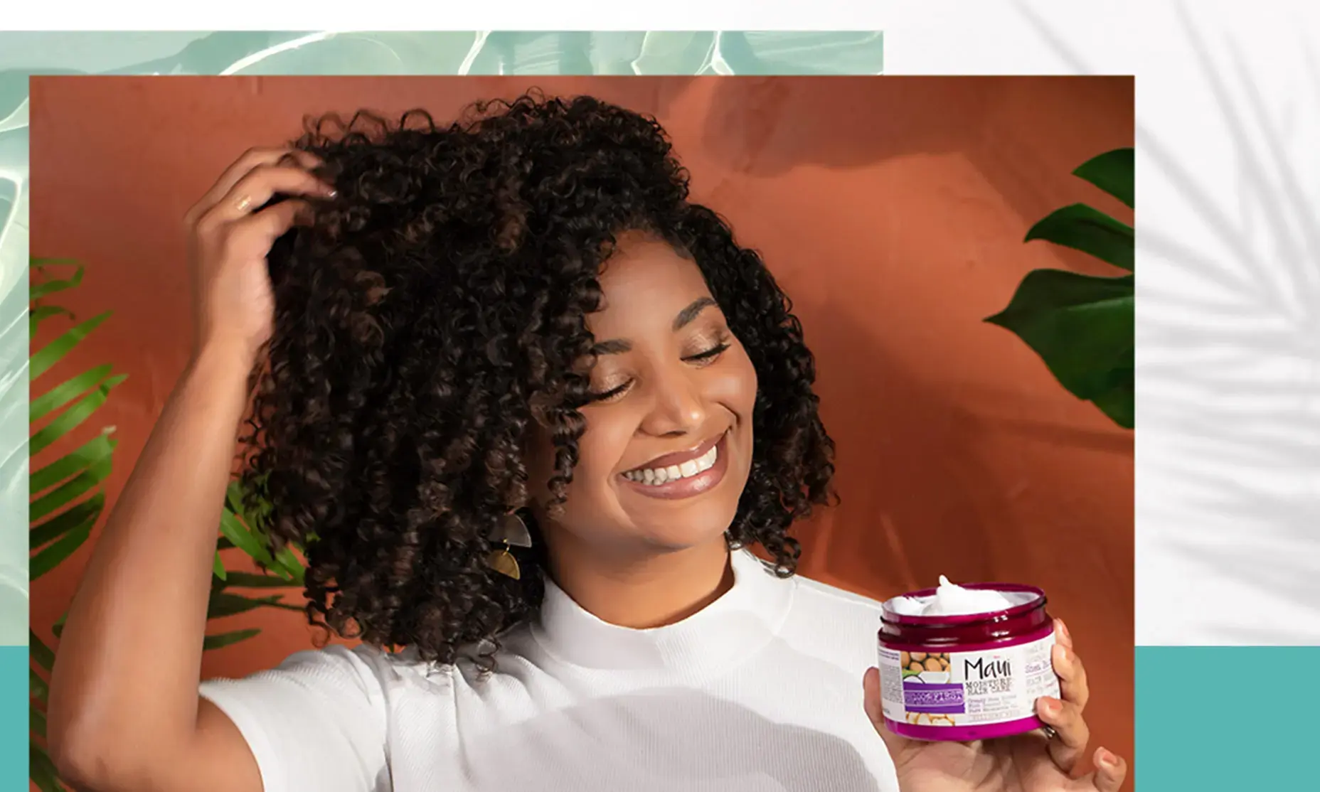 Woman with curly hair applying "Heal & Hydrate + Shea Butter Hair Mask" and smiling.