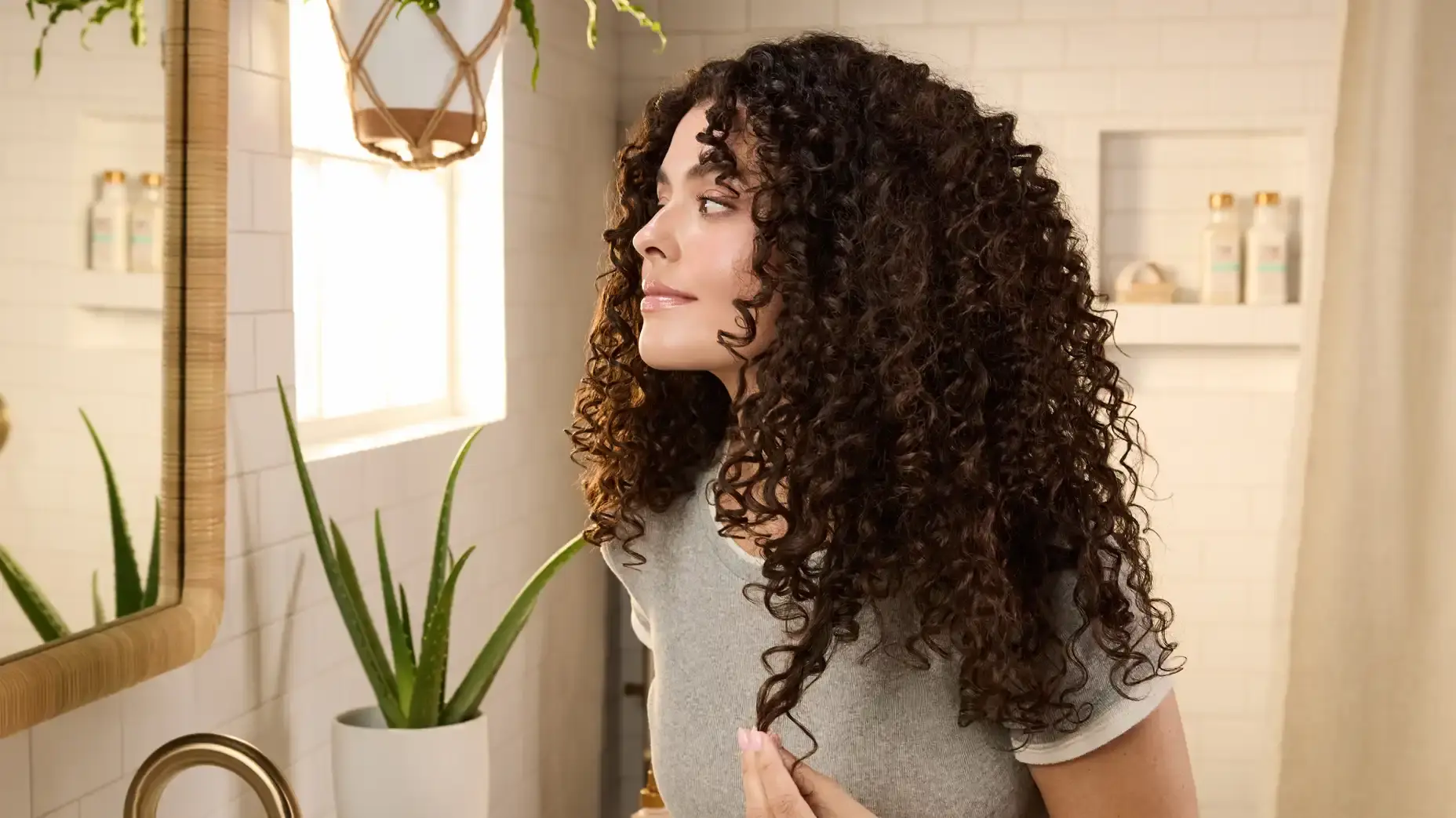 Smiling woman admiring curls after applying Maui Moisture® Scalp Care Serum