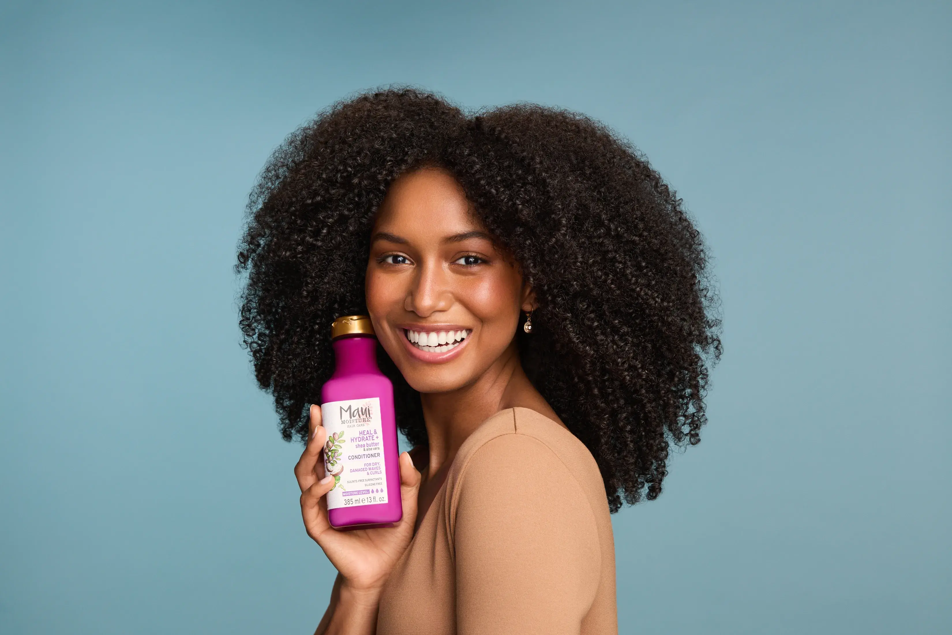 Woman with healthy curls holding Maui Moisture Heal and Hydrate Shea Butter Conditioner.