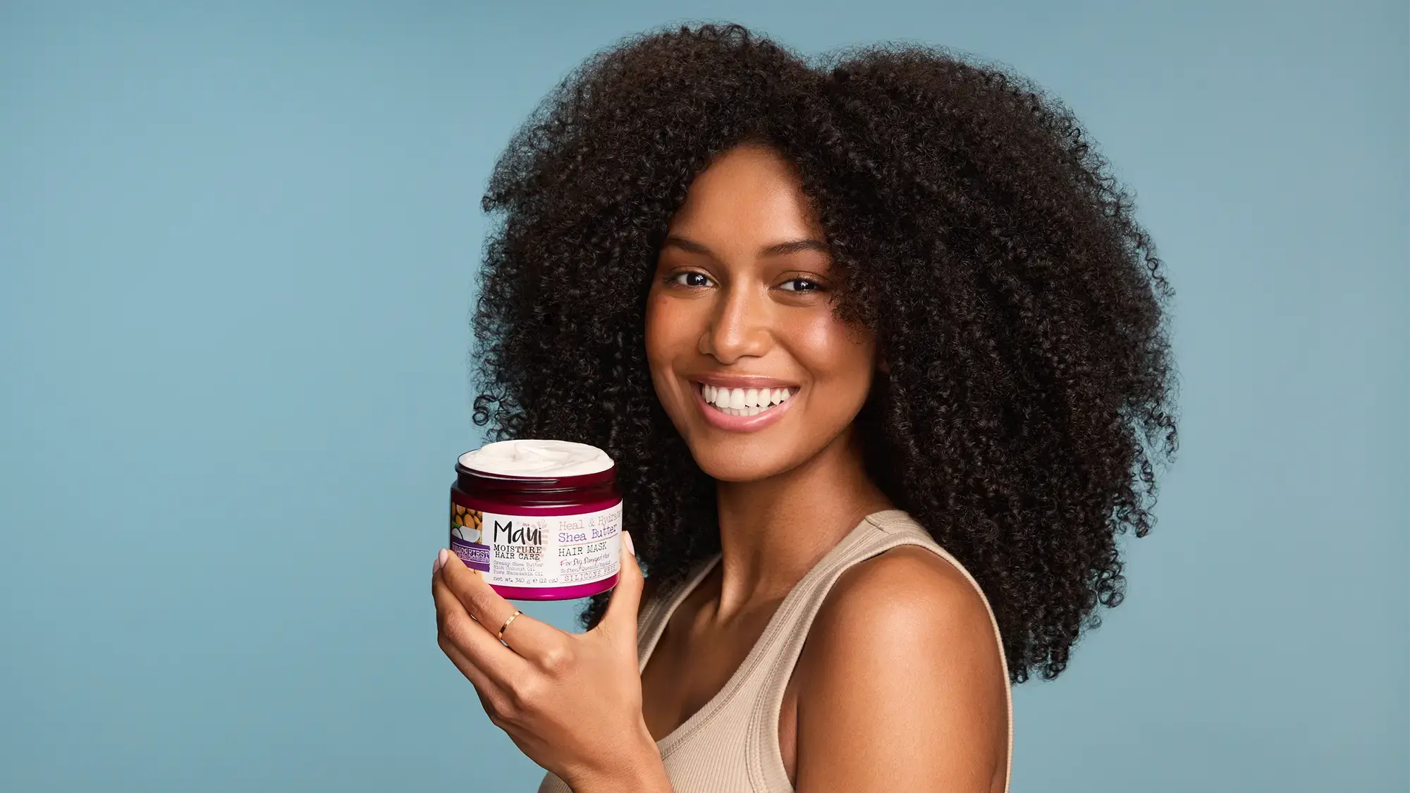 Woman with healthy curls holding Maui Moisture Shea Butter Hair Mask