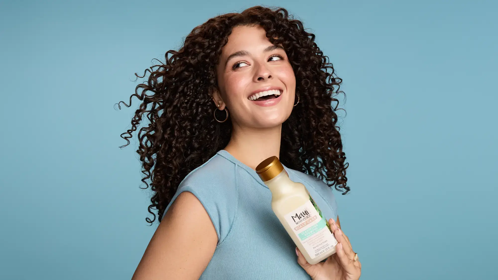 Smiling Woman with healthy curls holding Maui Moisture Scalp Care Clarifying Shampoo