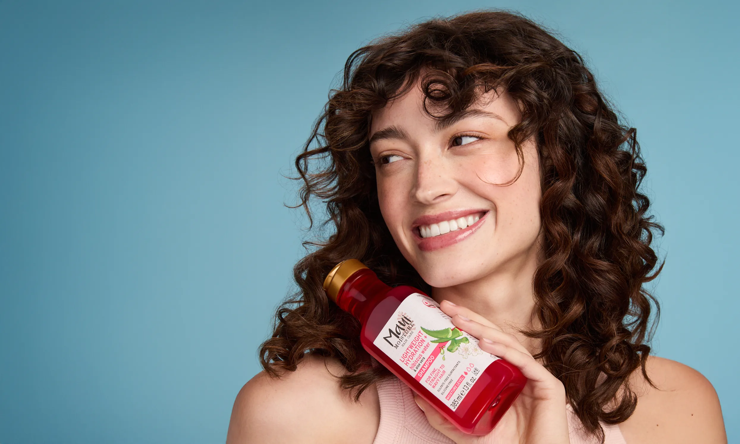 Woman smiling and holding bottle of Maui Moisture Hibiscus Water Shampoo