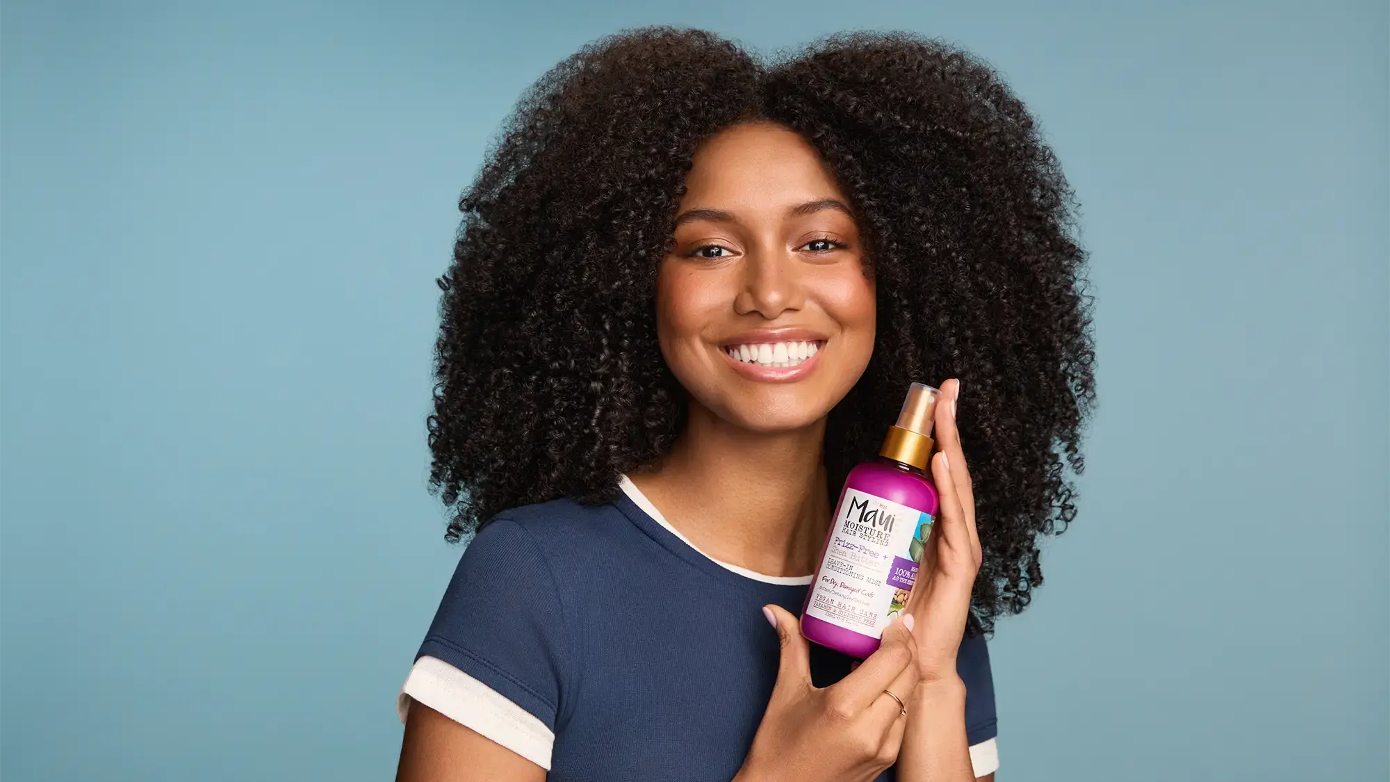 Woman with healthy curls holding Maui Moisture Shea Butter Leave In Mist