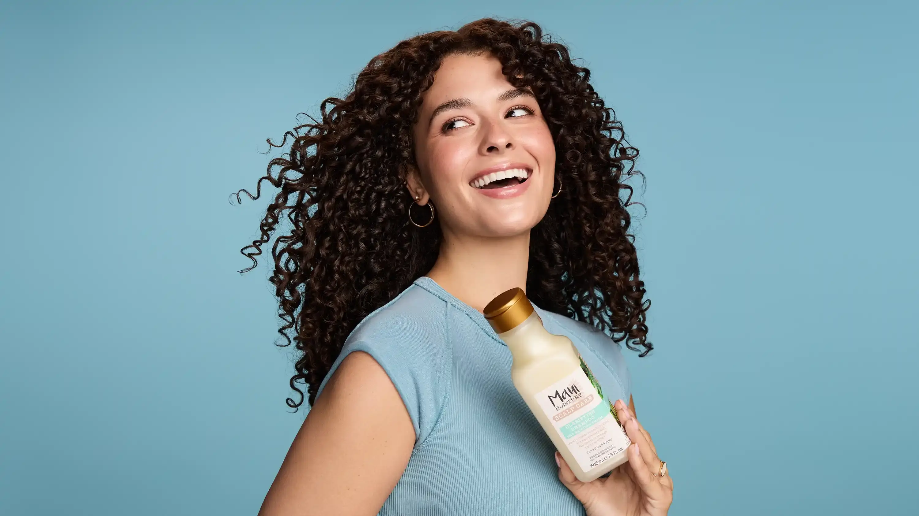 Smiling woman with curly hair holding Maui Moisture Scalp Care Clarifying Shampoo