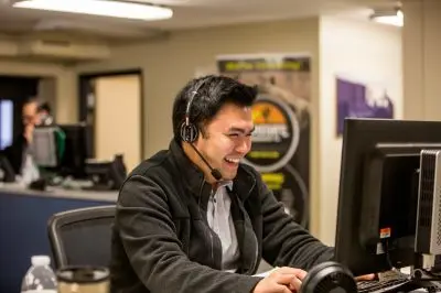 A person smiling while wearing a headset and working at a computer