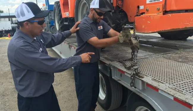 One person showing another person how to chain equipment to a truck bed