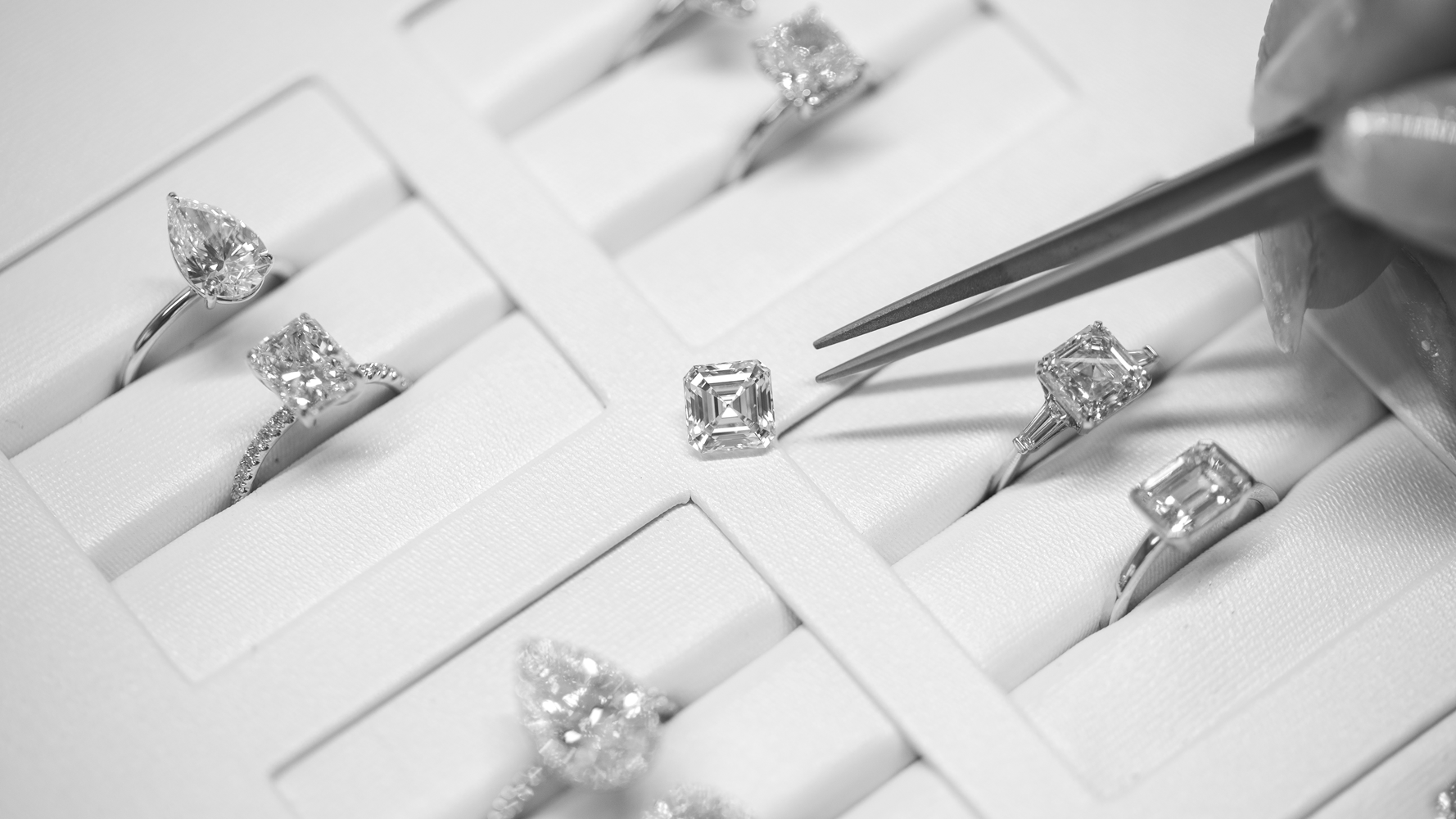 Tweezers reaching for loose asscher diamond amongst engagement rings