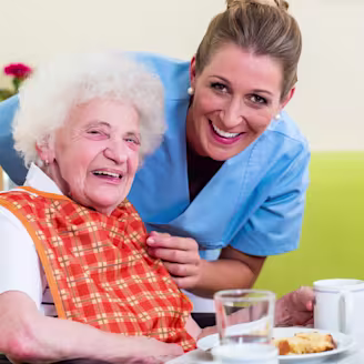 A care giver and an elderly person in a wheelchair smiling together