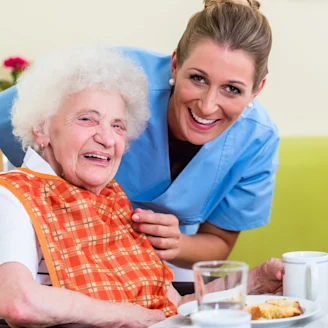 A care giver and an elderly person in a wheelchair smiling together