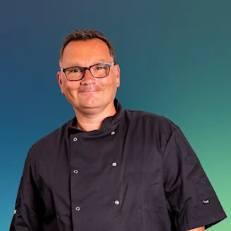 Paul Jennings headshot, Paul in black chefs jacket wearing glasses and smiling.