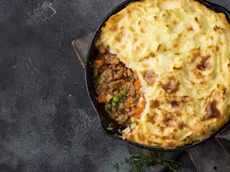 A cottage pie with some of the potato topping removed to show the Quorn inside