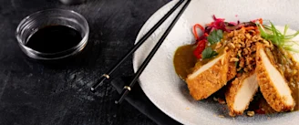 Quorn breaded chicken in white bowl with red chillis and green onion garnish with soy dipping sauce to left and black chopsticks 