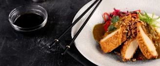 Quorn breaded chicken in white bowl with red chillis and green onion garnish with soy dipping sauce to left and black chopsticks