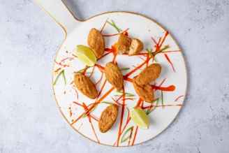 Quorn Vegan Chiqin Strips breaded chicken six pieces on white serving board with orange sauce and green onion garnish.