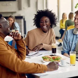 A group of three people laughing at a lunch table enjoying drinks and food