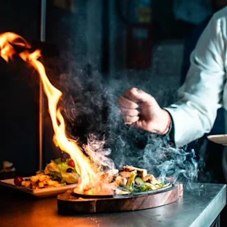 Flames from a dish of food with an outstretched arm in the background